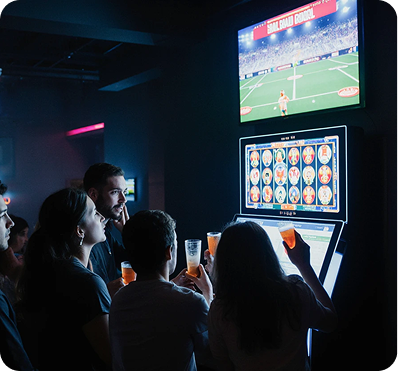 Grupo de personas jugando en máquinas recreativas con pantalla de fútbol al fondo